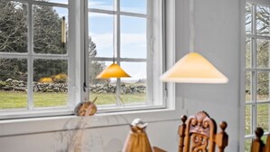 A dining area with a table, chairs, and a window with a view of a stone wall and trees. - Cozy home in Aakirkeby with WiFi (Aakirkeby)