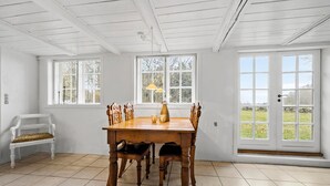 A dining room with a wooden table, chairs, and a bench. There are large windows and a door with a view of the outdoors. - Cozy home in Aakirkeby with WiFi (Aakirkeby)