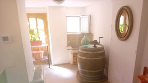A kitchen with wooden flooring, a wooden barrel, a sink, and a window with a view of greenery.