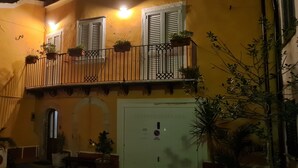 A yellow building with a balcony, potted plants, and a door with a sign.