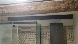 A bathroom with patterned tiles, a glass shower enclosure, and a wooden ceiling beam.