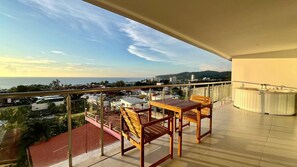 Un balcón con vista al mar y al paisaje urbano, con dos sillas de madera y una mesa.