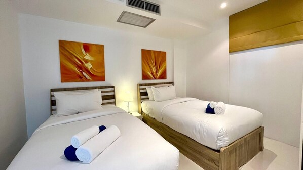 A hotel room with two beds, each with white linens and pillows, a wooden headboard, and two abstract paintings on the walls.