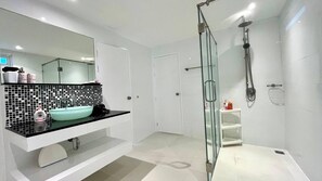 Un baño moderno con ducha de vidrio, lavamanos blanco y encimera negra, además de un salpicadero de azulejos.