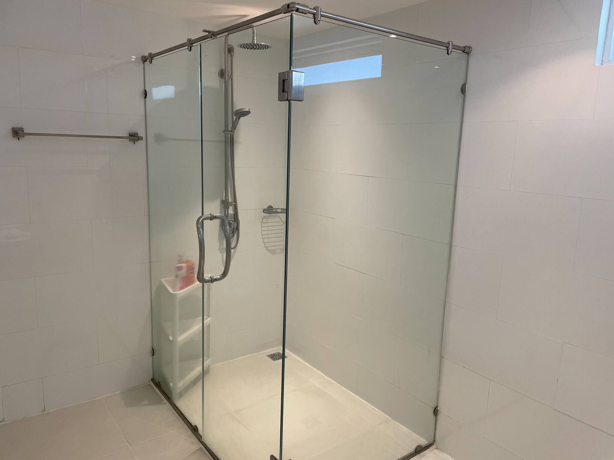 Cabina de ducha con paredes de vidrio, cabezal de ducha manual y rociador de mano.