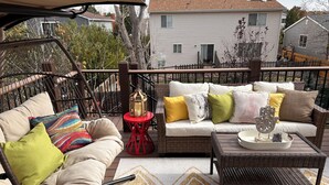Un patio techado al aire libre con un sofá de mimbre, cojines de colores, una mesita con un farolillo y una alfombra estampada.