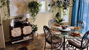 Un comedor con mesa de vidrio, sillas y plantas colgantes.
