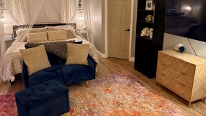 Un dormitorio con una cama, un sillón azul, un aparador de madera y un televisor.