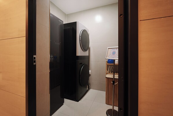 A compact laundry room with a washing machine and dryer, a small wooden cabinet, and a framed certificate on the wall. - WONJU CITI HOTEL Corporate City (Wonju)