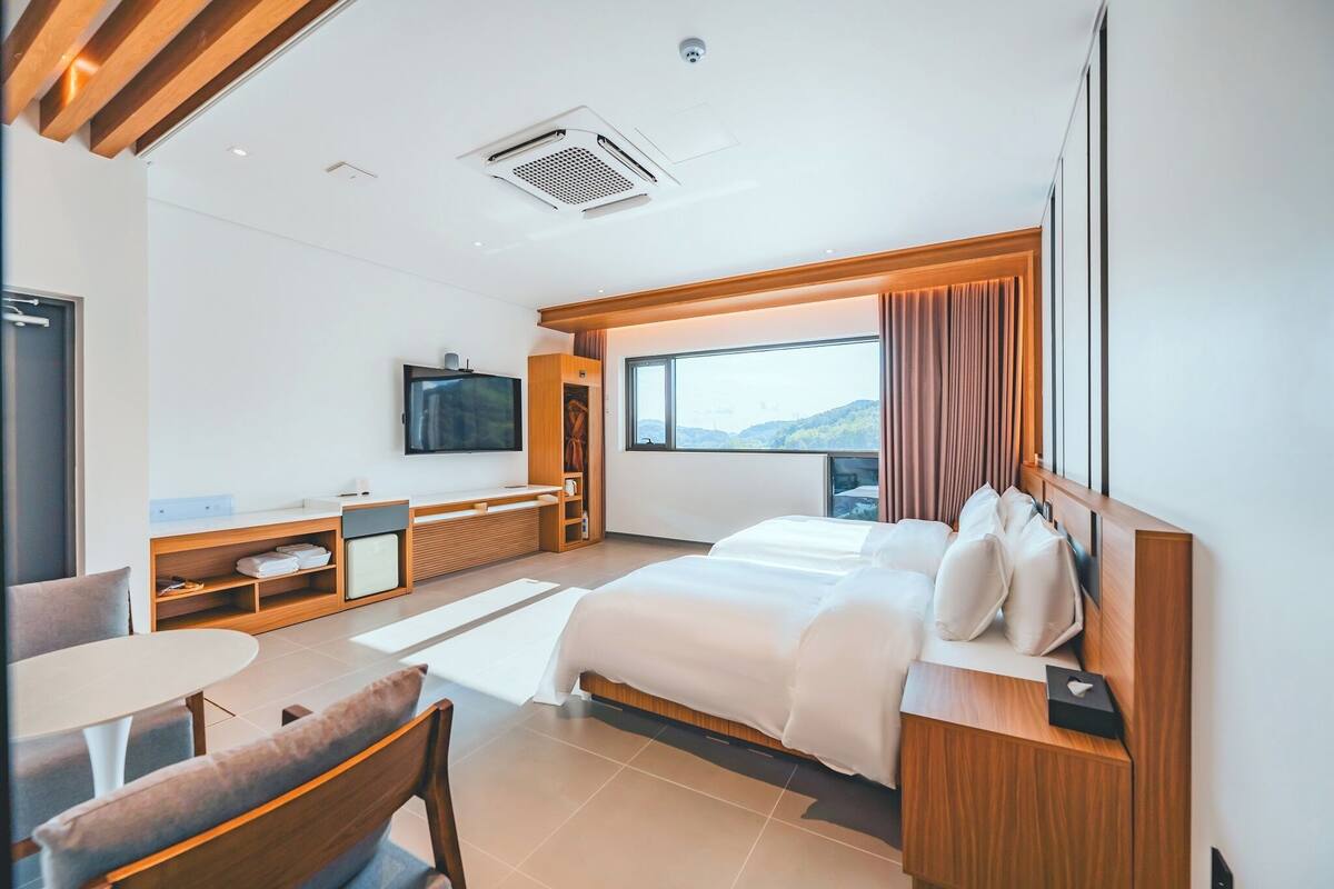 A modern hotel room with a large bed, a TV, a desk, and a view of the mountains.