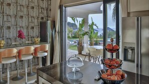 Una cocina moderna con una isla grande, taburetes de bar, una estantería y vistas al exterior.
