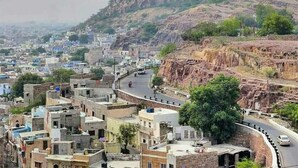 A cityscape with a prominent fort on a hill, surrounded by residential buildings and a winding road. - Guest House UGS  (Jodhpur)
