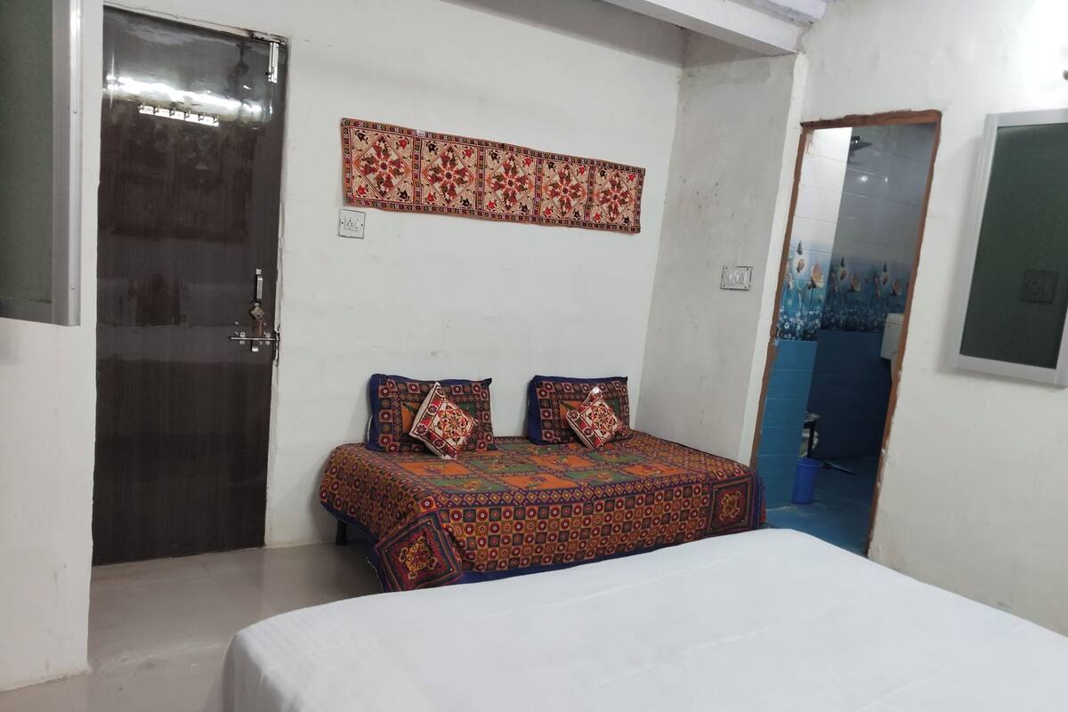A room with a bed, a door, a wall-mounted decorative piece, and a bathroom visible through an open door.