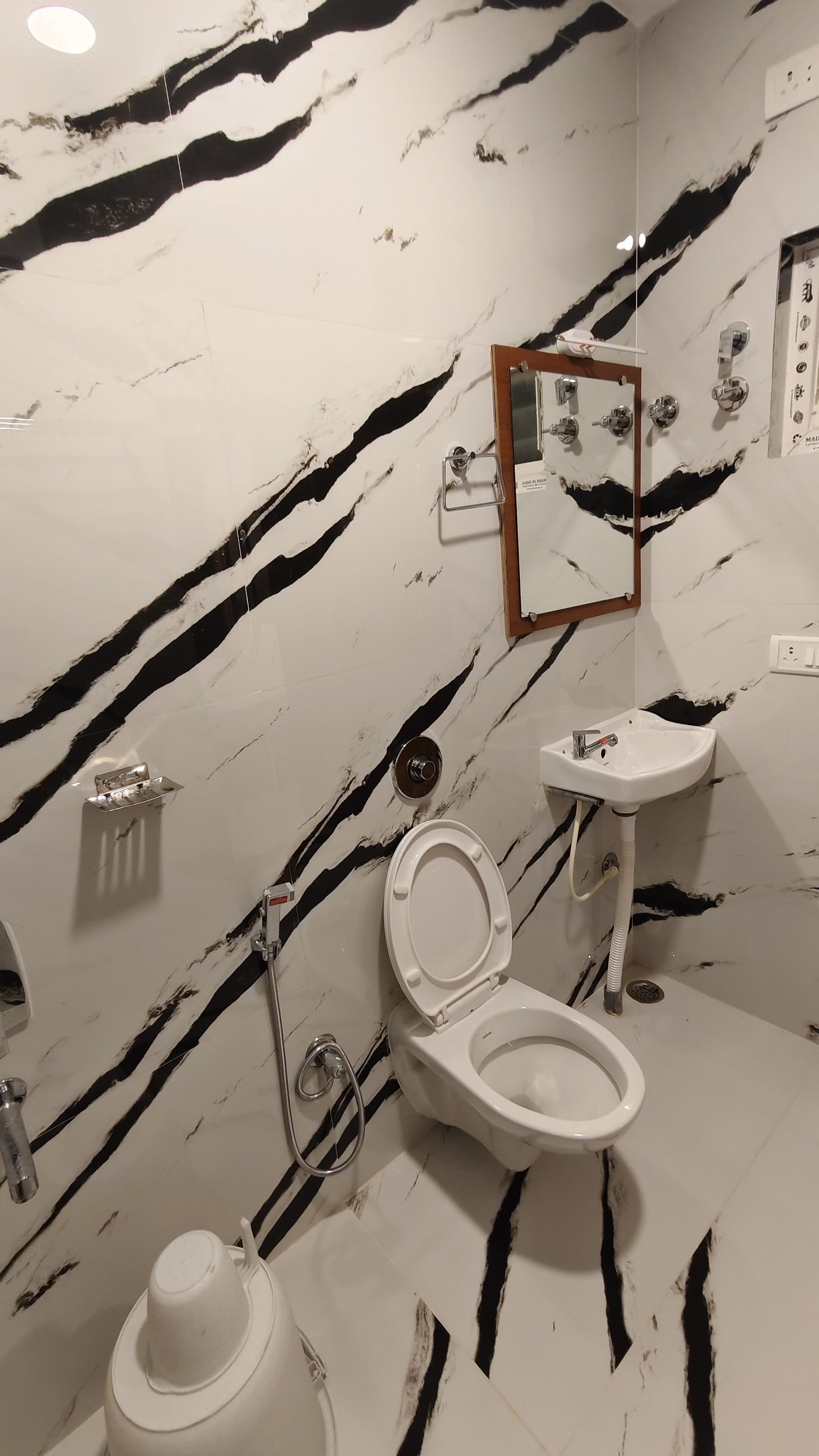 Un baño con piso y paredes de mármol blanco, inodoro blanco, lavamanos y ducha.