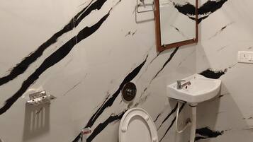 Un baño con piso y paredes de mármol blanco, inodoro blanco, lavamanos y ducha.