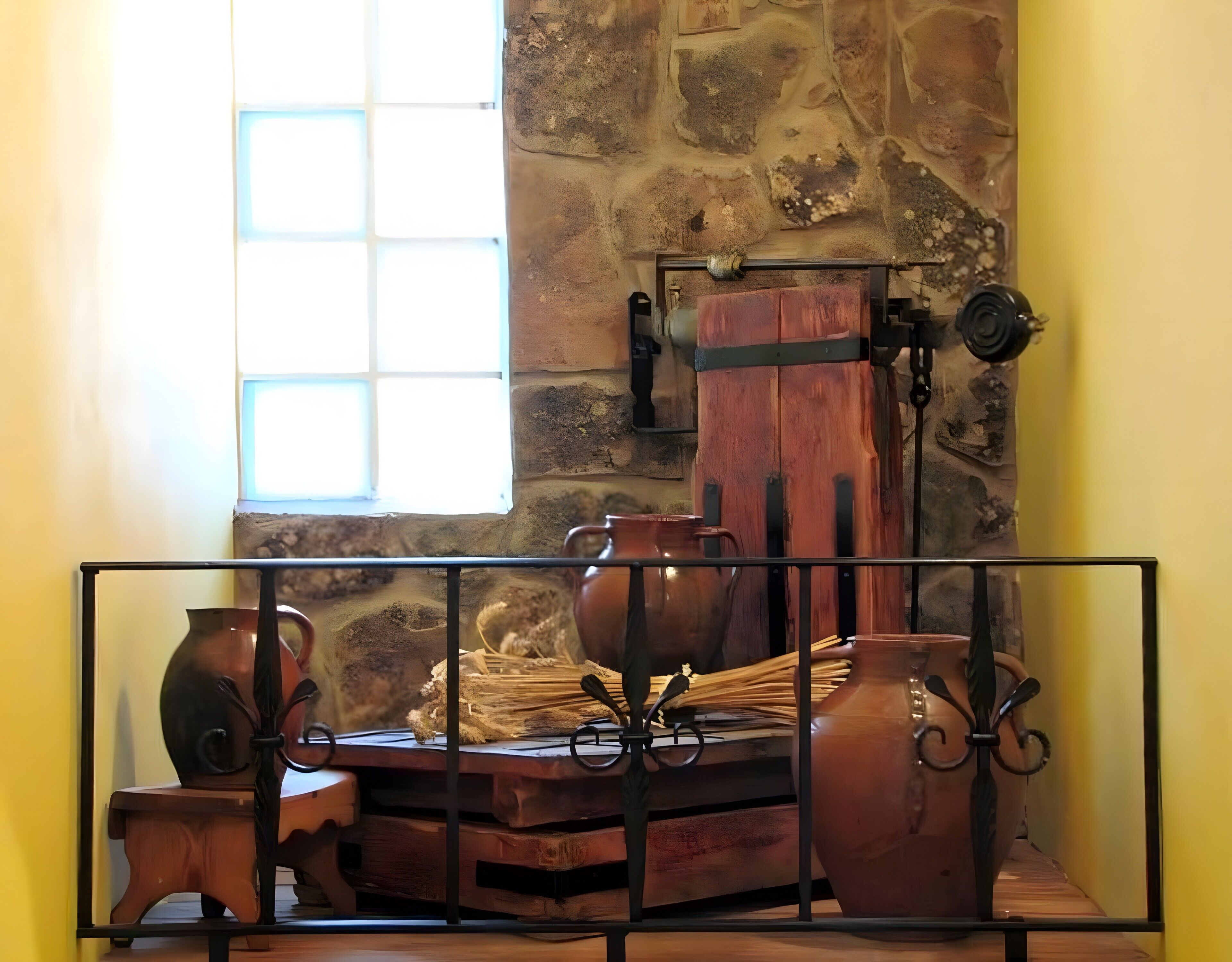 A rustic interior with a stone wall, a wooden table with pottery, and a window with natural light.