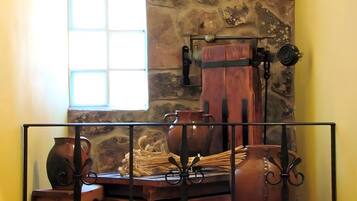 A rustic interior with a stone wall, a wooden table with pottery, and a window with natural light.