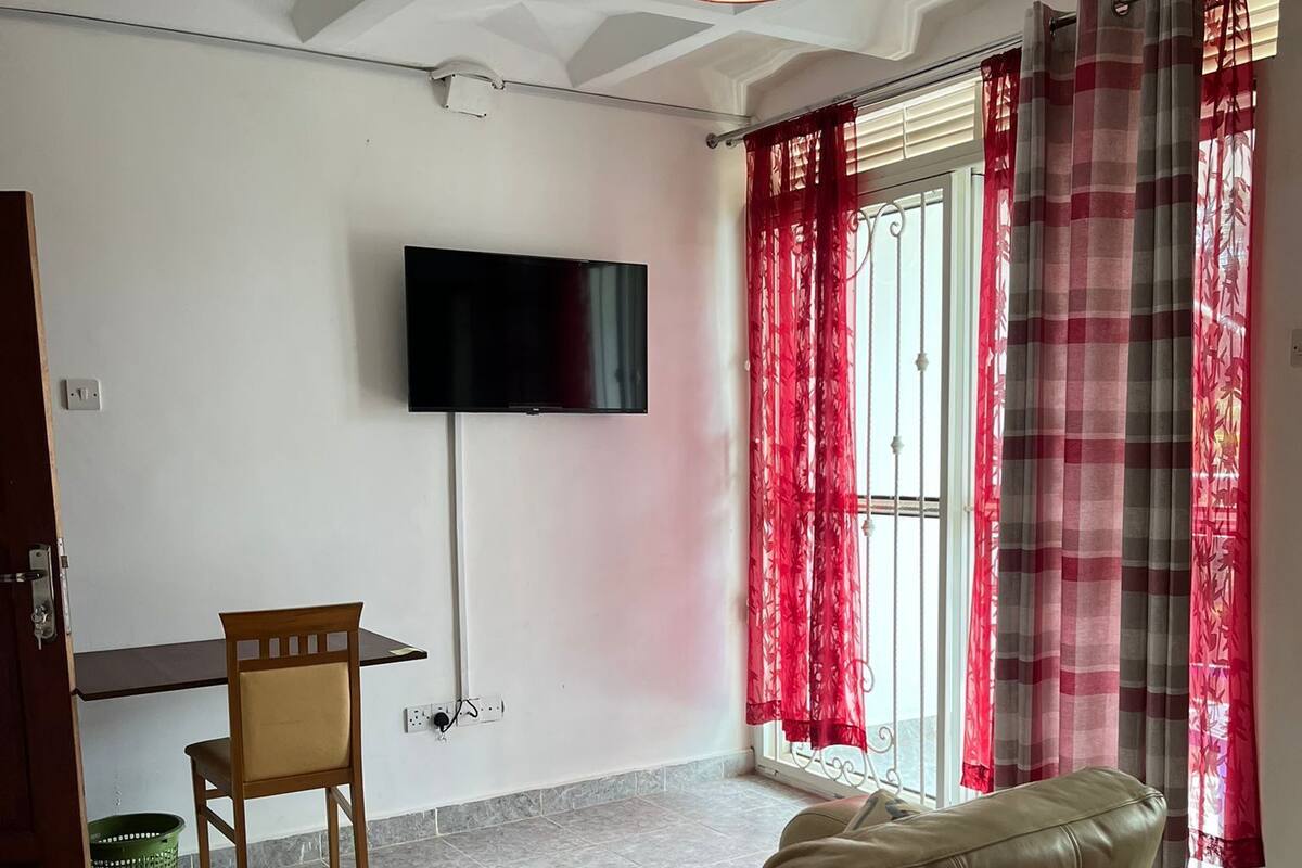 A hotel room with a sofa bed, a television mounted on the wall, a desk, and a chair.