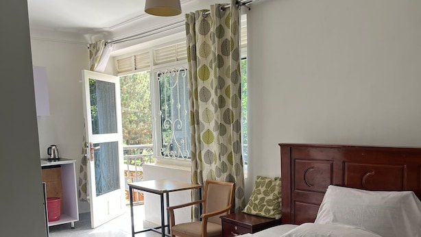 Une chambre à coucher avec un lit, une tête de lit en bois, une fenêtre avec des rideaux, une table et une chaise.