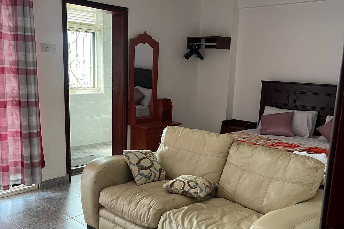 A room with a leather sofa, a bed with a headboard, a mirror, and a hanging red light fixture.