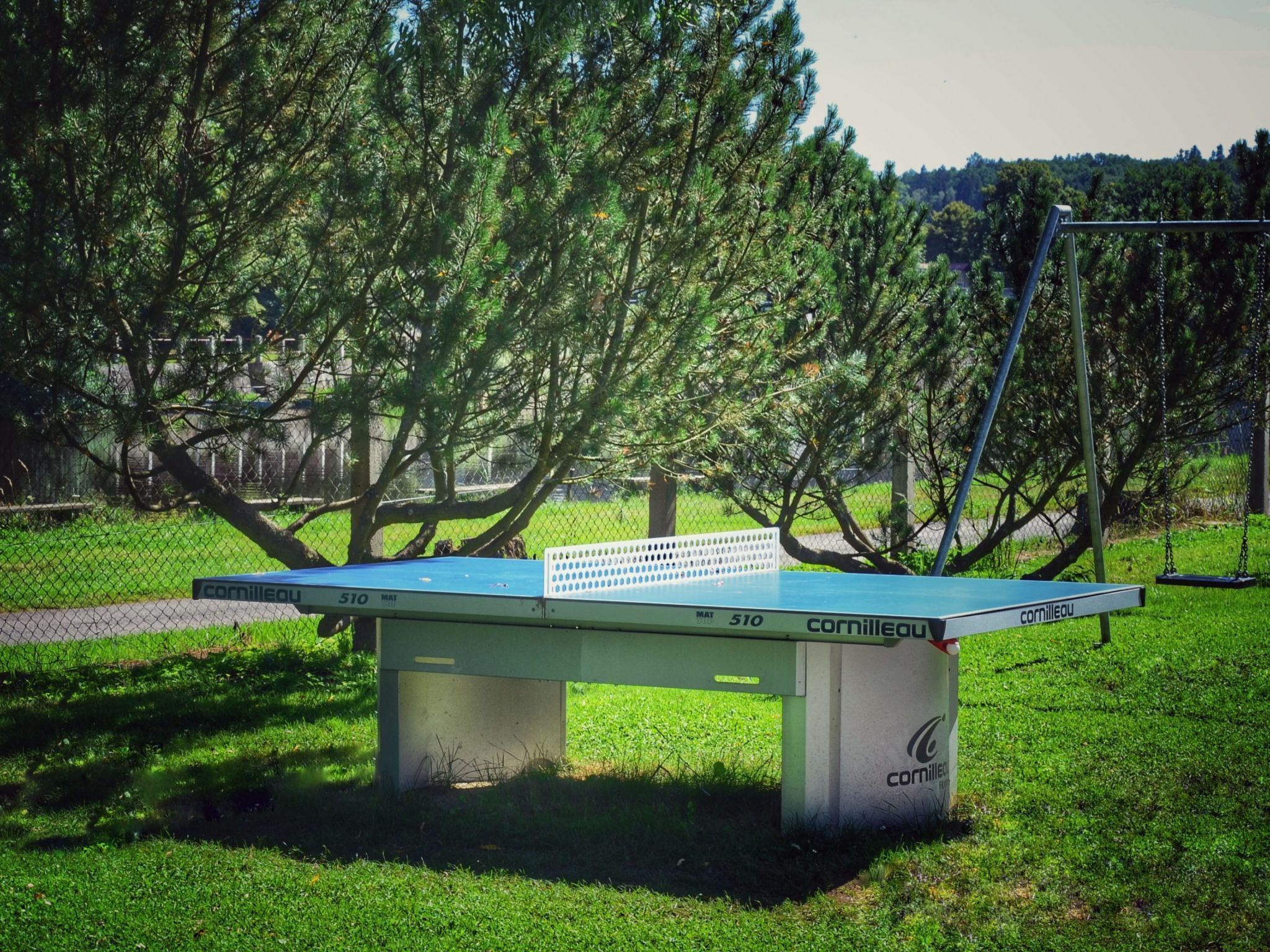 Una mesa de ping pong en un parque con estructura metálica y superficie de juego verde.
