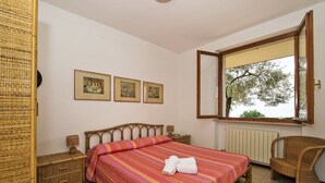 A bedroom with a bed, a chair, a window, and three framed pictures on the wall.