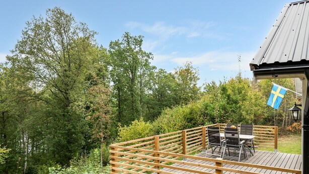 Una terraza de madera con mobiliario exterior, rodeada de abundante vegetación y árboles.