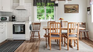 Cocina con armarios blancos, estufa y microondas. Hay una mesa de comedor con sillas de madera y una ventana con vista a zonas verdes.