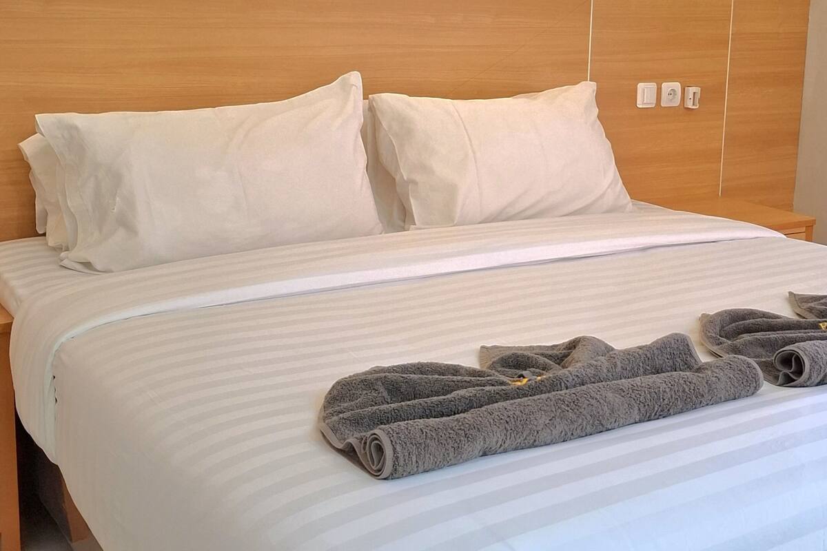 Una cama bien hecha con sábanas blancas y dos almohadas, un cabecero de madera y dos toallas enrolladas sobre la cama.