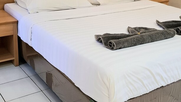 A neatly made bed with white linens, a wooden headboard, and a nightstand with a lamp. - Royal Kencana Hotel (Jepara)