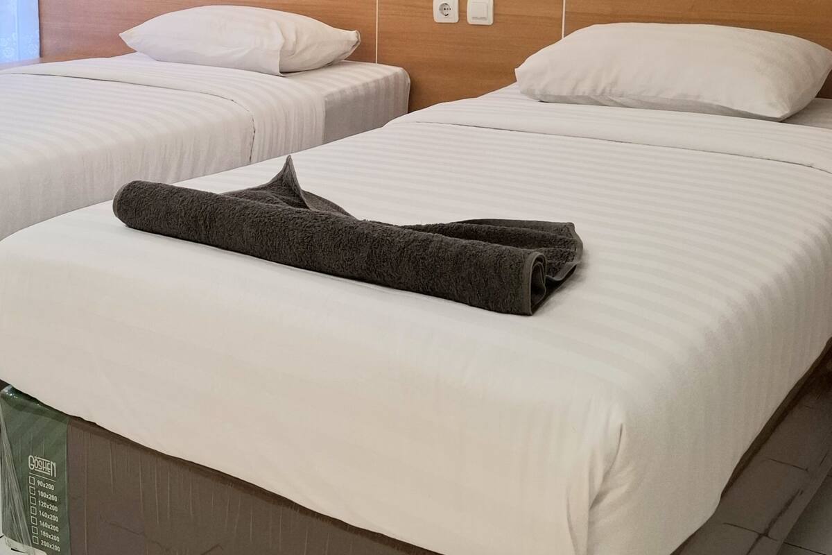 Habitación de hotel con dos camas, cada una con ropa de cama y almohadas blancas, y una toalla gris sobre la cama en primer plano.