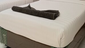 A hotel room with two beds, each with white bedding and pillows, and a grey towel on the bed in the foreground. - Royal Kencana Hotel (Jepara)