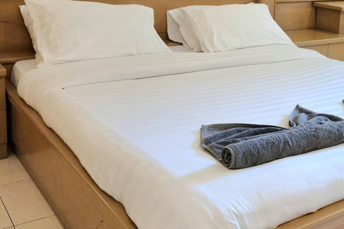 Una cama bien hecha con sábanas blancas y una toalla gris enrollada encima.