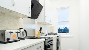 A kitchen with white cabinets, a stove, a toaster, and a window with a view of buildings. - Court Street by Central Serviced Apartments (Dundee)