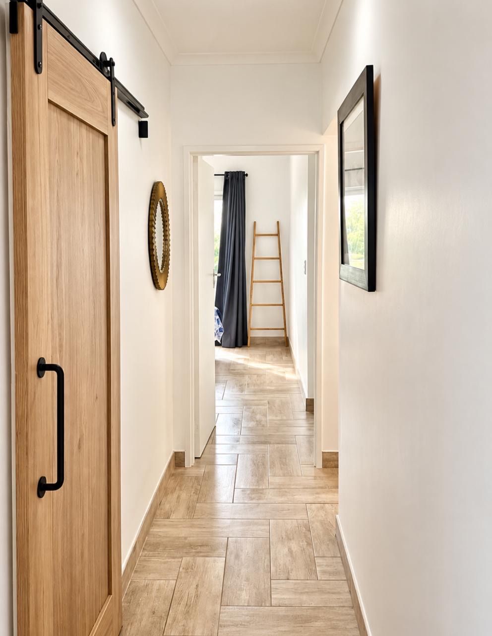 Un couloir avec une porte en bois, une échelle et un tableau encadré accroché au mur.