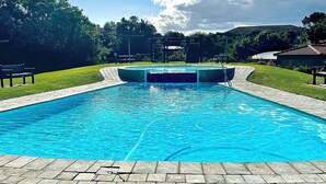 A rectangular swimming pool with a clear blue water surface, surrounded by a paved walkway and a grassy area. - Charming 2-bedroom apartment in the beautifully designed Gary Player Golf Estate (Plettenberg Bay)
