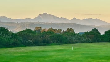 Un terrain de golf avec une clôture en bois au premier plan, un ciel dégagé et des montagnes en arrière-plan.