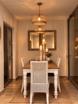 Un coin repas avec une table en bois, des chaises en osier blanches, un chandelier central et un luminaire suspendu.