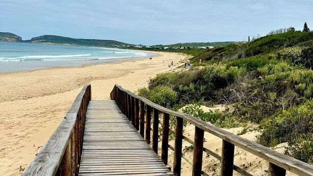 A wooden boardwalk leading to a sandy beach with a view of the ocean and distant hills. - Charming 2-bedroom apartment in the beautifully designed Gary Player Golf Estate (Plettenberg Bay)