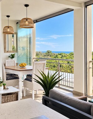 Een balkon met uitzicht op zee, met rieten meubilair en een eethoek met een tafel en stoelen.