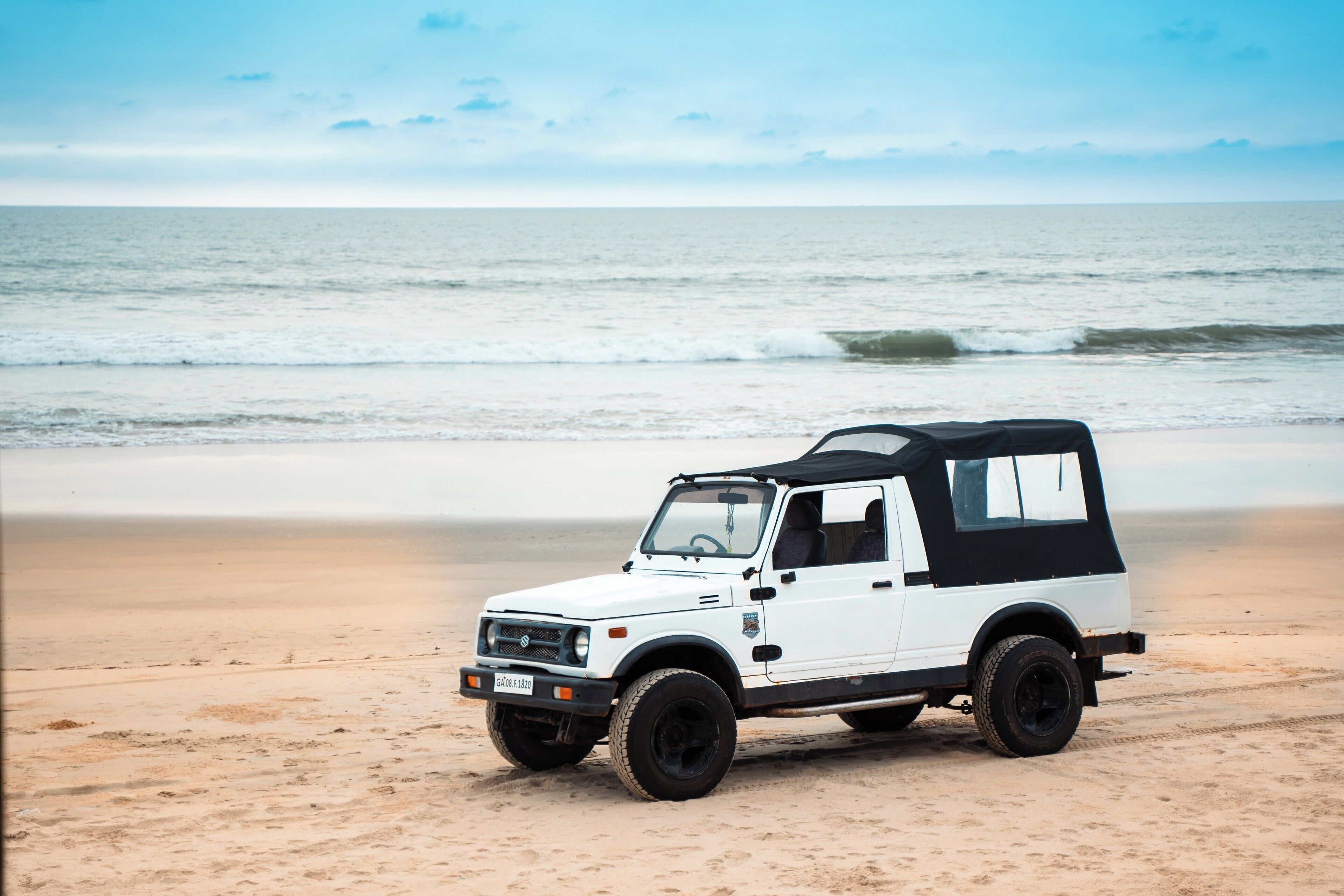 Un vehículo todoterreno blanco estacionado en una playa arenosa, con el océano al fondo.