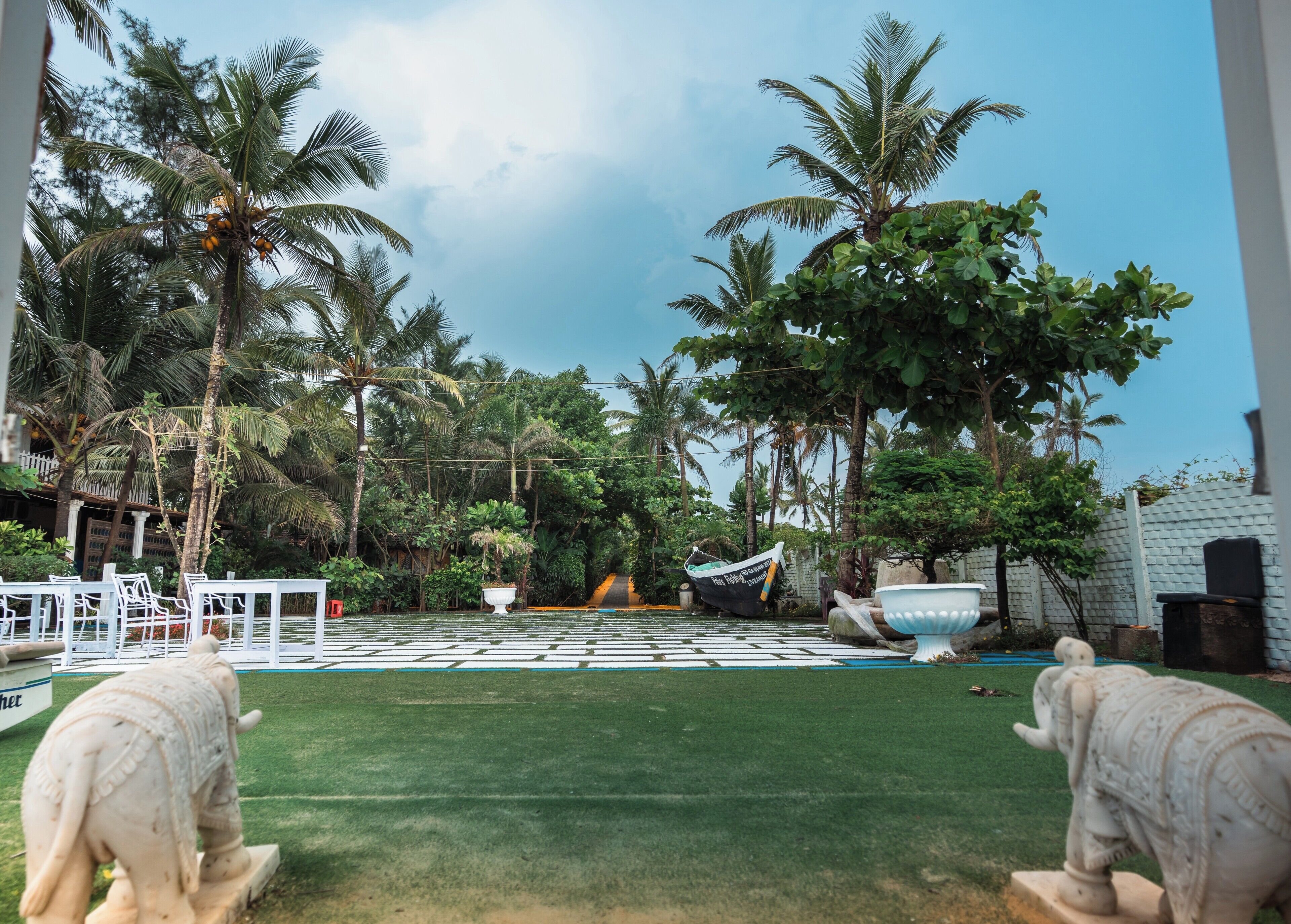 A tropical garden with palm trees, a pool, and two elephant statues.