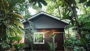 A small, dark-colored wooden house surrounded by lush greenery. - Nasya Beachside Cottages (Benaulim)