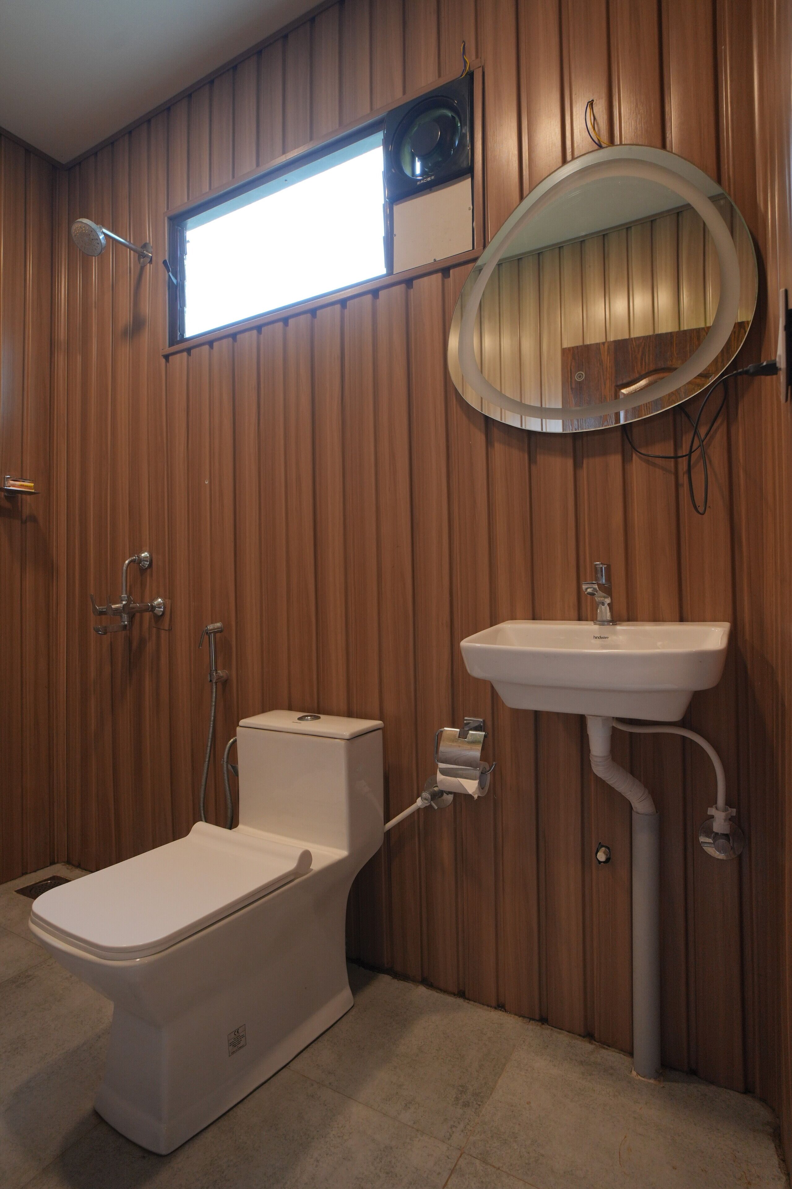 A bathroom with wooden paneling, a toilet, a sink, a mirror, and a window.