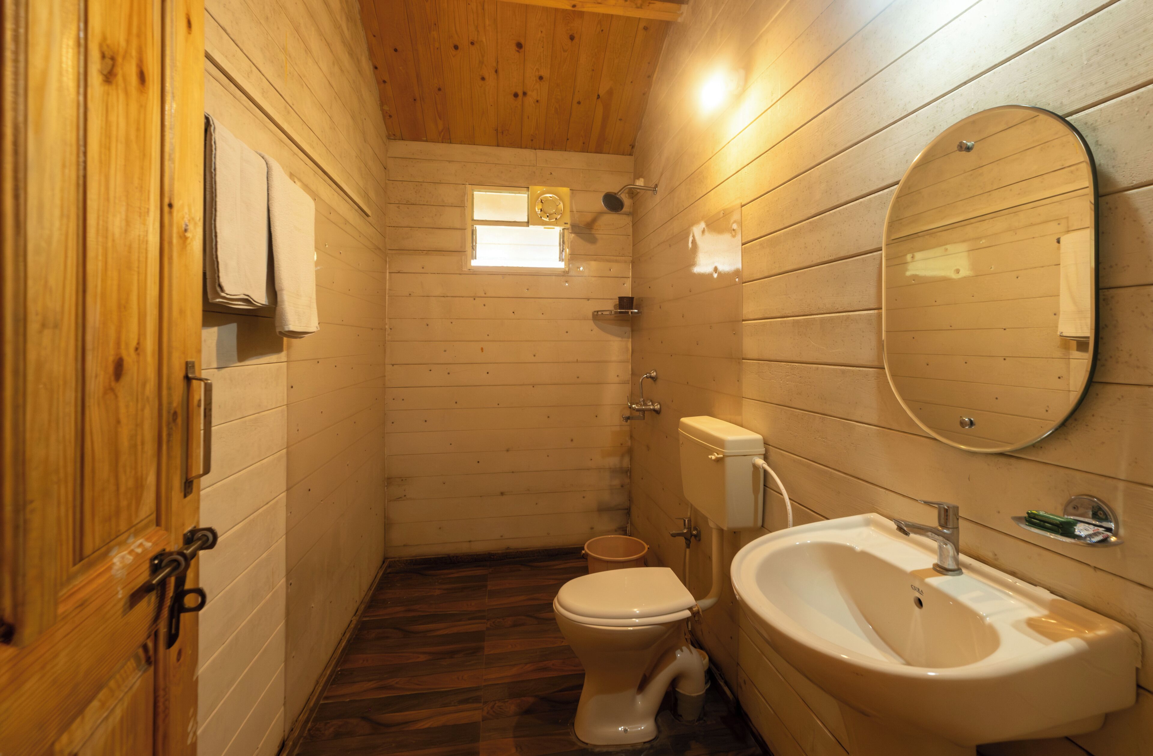 Un baño con paneles de madera, un inodoro, un lavamanos y un ventanal pequeño.