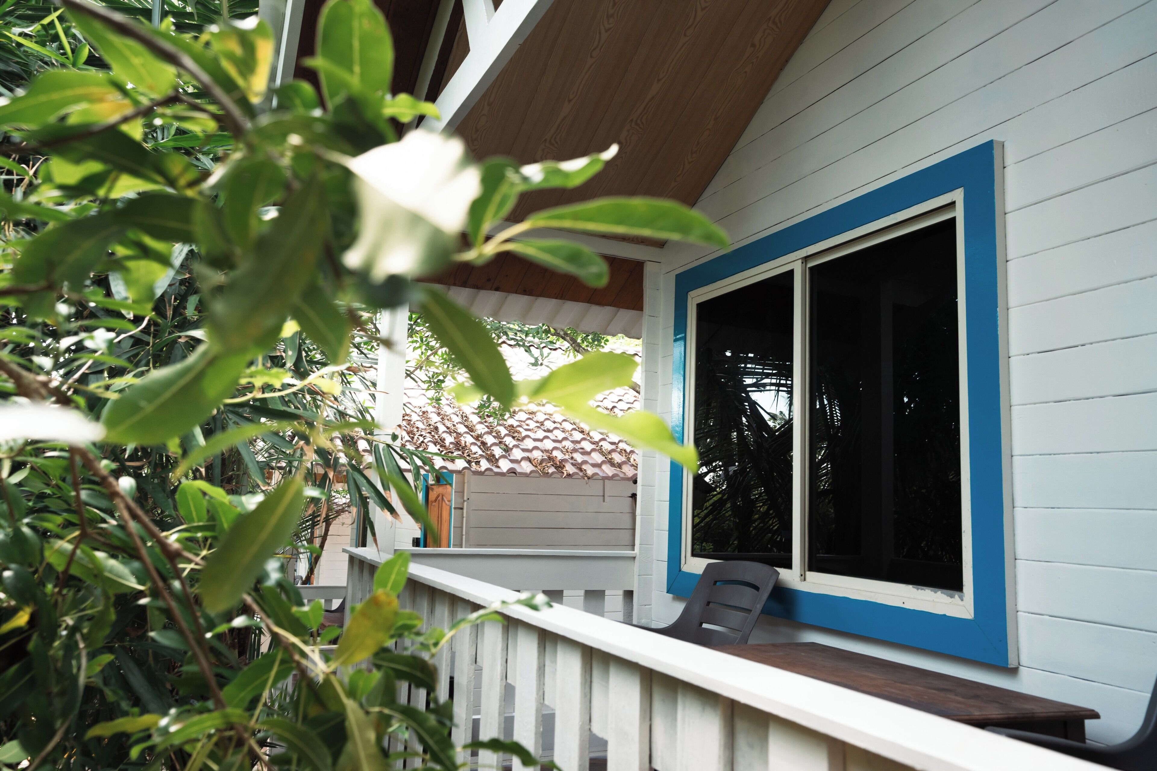 A wooden deck with a white railing, a bench, and a window with blue trim.