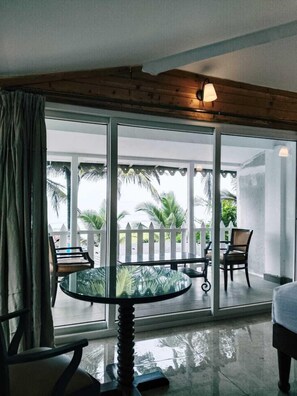 A room with a glass table and chairs, large sliding glass doors leading to a balcony with a white fence and palm trees.