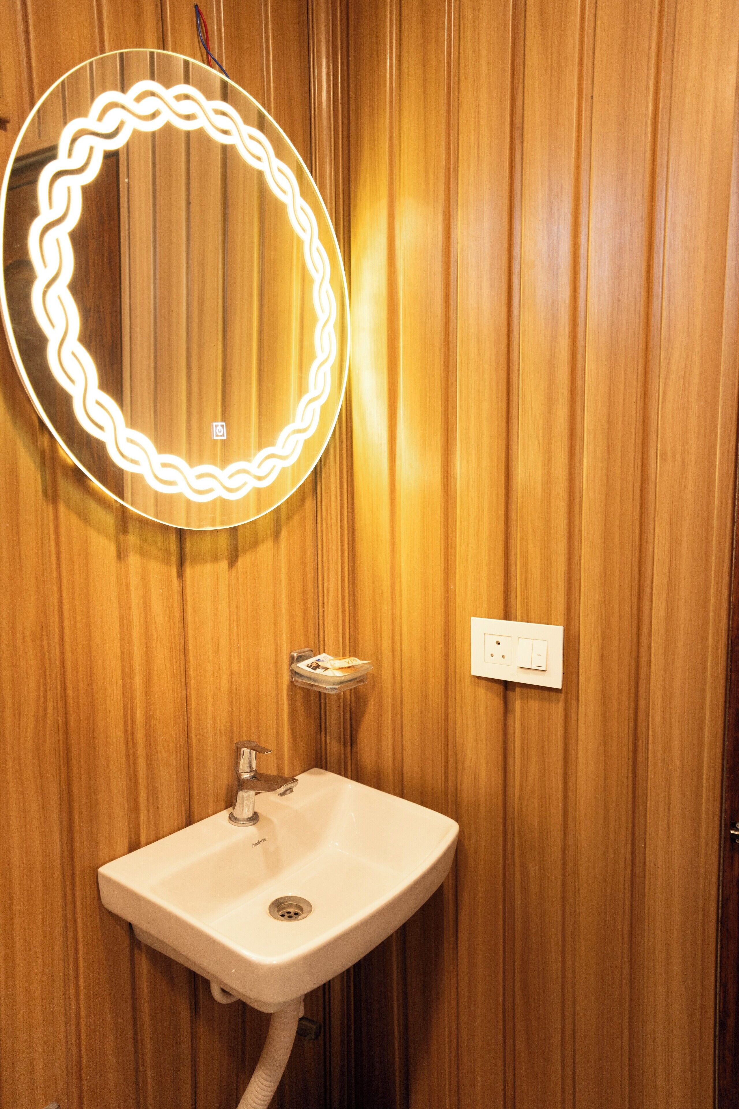 Un baño con pared de madera, un lavabo, un espejo con iluminación y un enchufe.