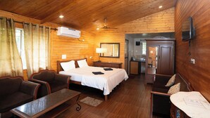 A wooden cabin-style room with a bed, two sofas, a table, and a TV. - Nasya Beachside Cottages (Benaulim)