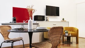 A modern kitchen with a dining table, wicker chairs, a red accent wall, a flat-screen TV, and a small side table. - Easylife-Sophisticated  with Jacuzzi in Centrale (Milano)